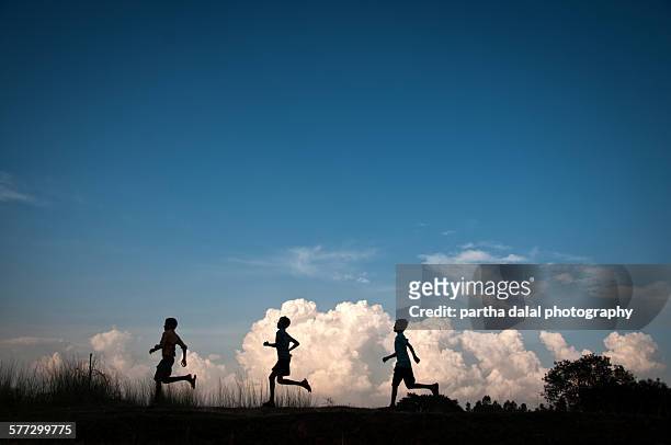kids running in clouds silhouette - village boy foto e immagini stock