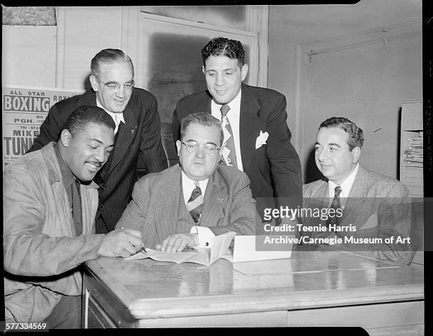 Boxer Bob Baker signing contract, surrounded by TW Stephen, Anthony 'Cowboy' DeLuca, William Bettor, and another man, in office, Pittsburgh,...