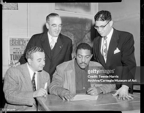 William Bettor, TW Stephen, and Anthony 'Cowboy' DeLuca, surrounding boxer Bob Baker signing contract, in office, Pittsburgh, Pennsylvania, October...
