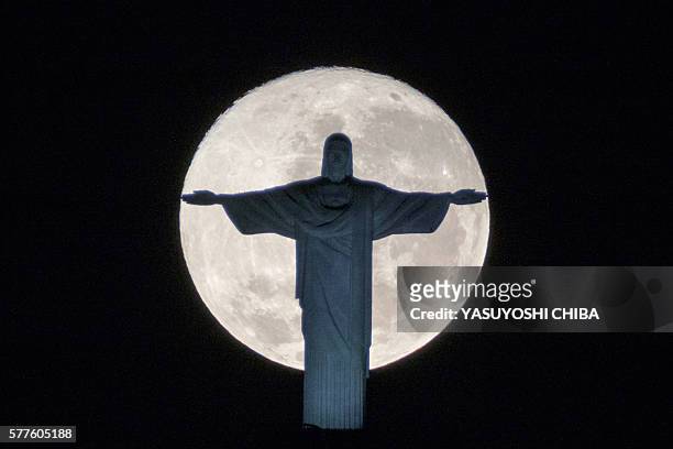 The silhouette of the statue of Christ the Redeemer atop Corcovado hill stands out against the full moon in Rio de Janeiro, Brazil, on July 19, 2016....