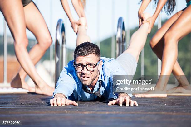 femmes tirant un homme sur la terrasse de la piscine - trainee photos et images de collection