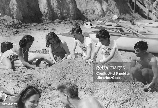 Student Life, Beach Party, Senior Week Candid shot of students & their girlfriends burying a student in the sand at Triton beach, 1947.