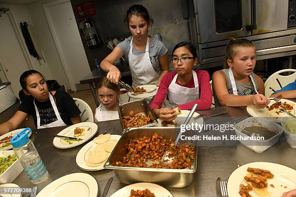 Taryn Bowman middle in gray t-shirt and white apron, serves herself some spicy turky and yam taco mix after she and the other girls prepared the...