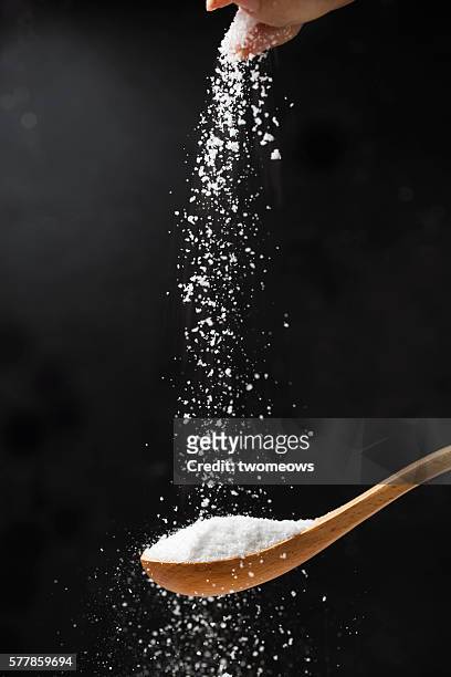 salt in wooden spoon on black background. - falling food stock pictures, royalty-free photos & images