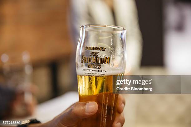 Member of the media holds a glass of Suntory Holdings Ltd.'s The Premium Malt's Pilsner beer at the company's Master House bar in Hong Kong, China,...