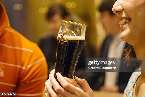 Member of the media holds a glass of Suntory Holdings Ltd.'s The Premium Malt's Black beer at the company's Master House bar in Hong Kong, China, on...