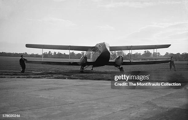 Two men at an Aerodrome holding the wing tip on either side of a de Havilland DH.84 Dragon a successful small commercial aircraft designed and built...