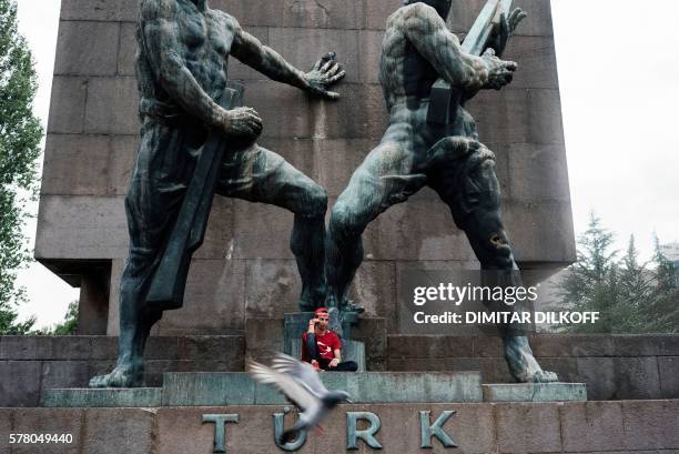 Pigeon flies past a man wearing a Turkish flag over his shoulders sitting at the foot of the Guven Monument off the main Kizilay Square in Ankara on...