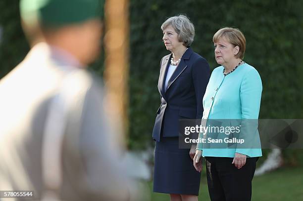 German Chancellor Angela Merkel and British Prime Minister Theresa May listen to a guard of honor play their nations' respective national anthems...
