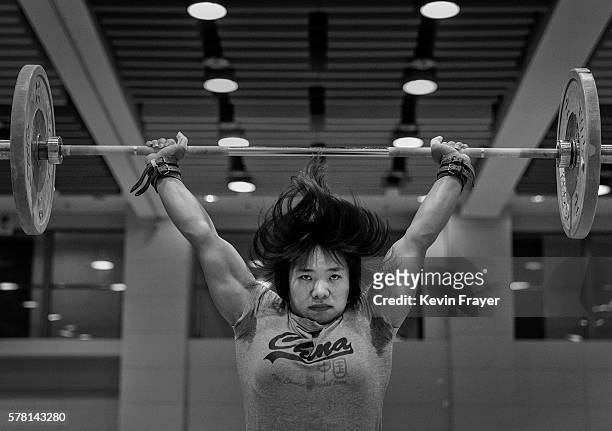 Chinese female weightlifter Xiang Yanmei, who competes in the 69 kg weightclass, rests with a weight on her stomach as she checks her phone during a...