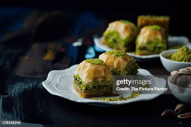 pistachio baklava slices served on two plates along with a bowl of whole pistachio and  a bowl of ground pistachio. - pistachio stock pictures, royalty-free photos & images