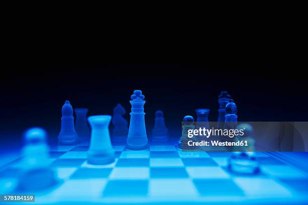 chess pieces on blue glass board against dark background - chess strategy stock pictures, royalty-free photos & images