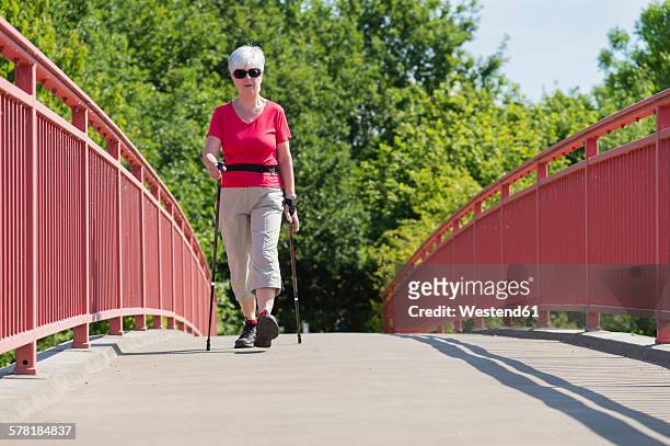senior woman doing nordic walking over a footbridge - mobility walker stock-fotos und bilder