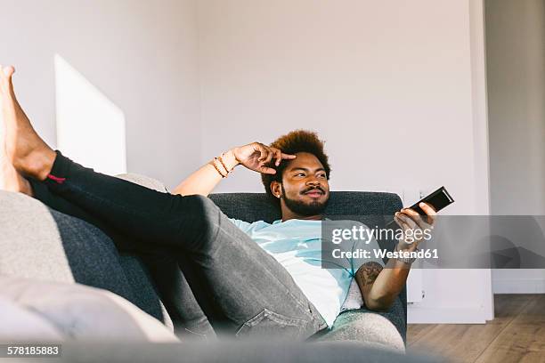 young man lying on couch watching tv - regarder tv photos et images de collection
