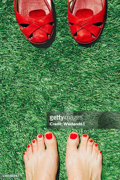 barefoot women with nails painted red next to a pair of red shoes, on the green grass - red nail polish stockfoto's en -beelden