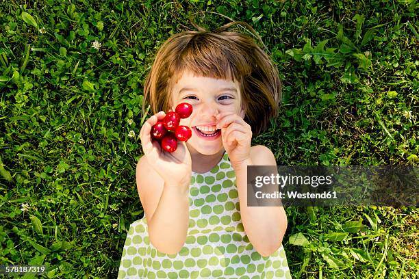 smiling little girl with cherries lying on a meadow - german girl alone stock pictures, royalty-free photos & images