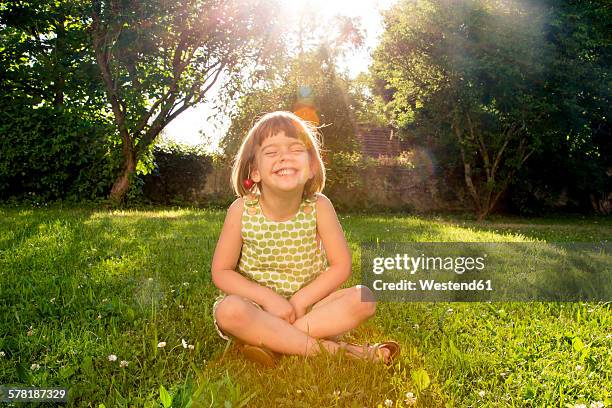 little girl wearing cherries sitting on a meadow at backlight - pernas cruzadas imagens e fotografias de stock