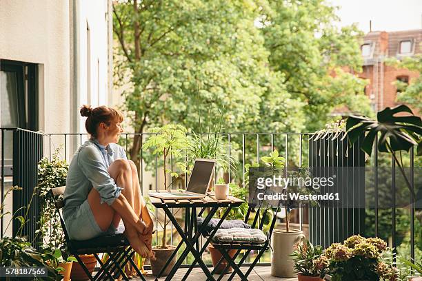 smiling woman looking at her laptop on balcony - balkon stockfoto's en -beelden