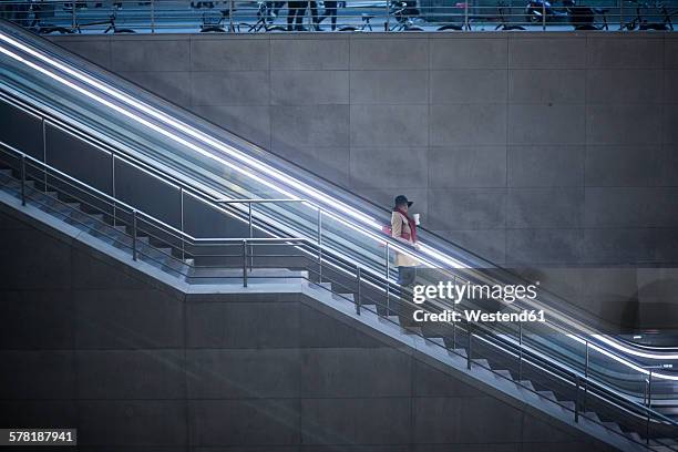 young woman with coffee to go standing on escalator - rolltreppe stock-fotos und bilder