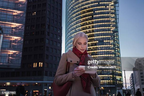 germany, berlin, young woman with mini tablet in the evening at potsdam square - potsdamer platz photos et images de collection