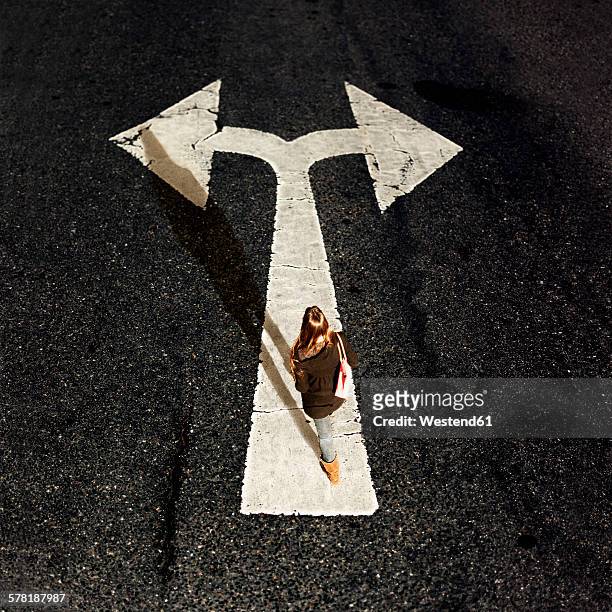 woman walking on directional arrow of a road - entscheidung stock-fotos und bilder