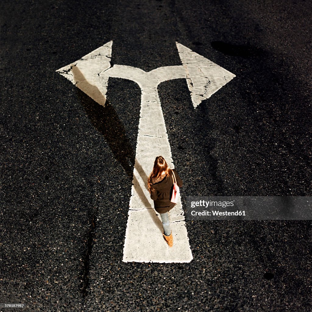 Woman walking on directional arrow of a road