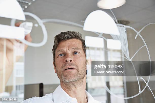 businessman drawing diagrams on glass pane in office - strategie stock-fotos und bilder