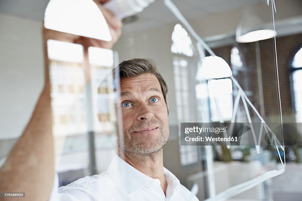 Businessman drawing diagram on glass pane in office