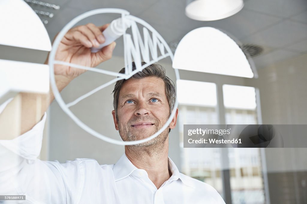 Businessman drawing diagram on glass pane in office