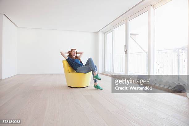 young woman sitting on yellow armchair in her empty living room - sedia foto e immagini stock