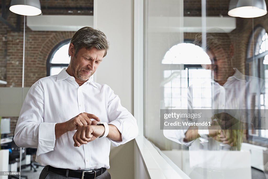 Smiling businessman in office looking at smartwatch