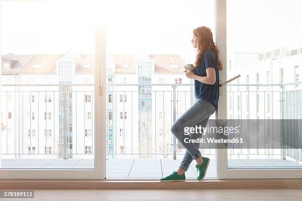 young woman leaning at sliding door of balcony looking at distance - open day 1 stock pictures, royalty-free photos & images