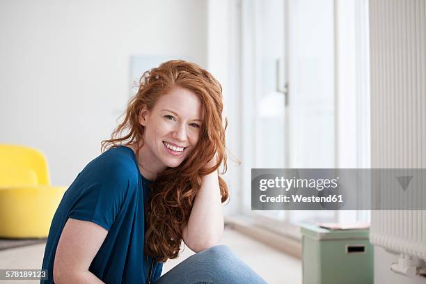 portrait of happy young woman sitting on the floor of her living room - hand in hair stock pictures, royalty-free photos & images