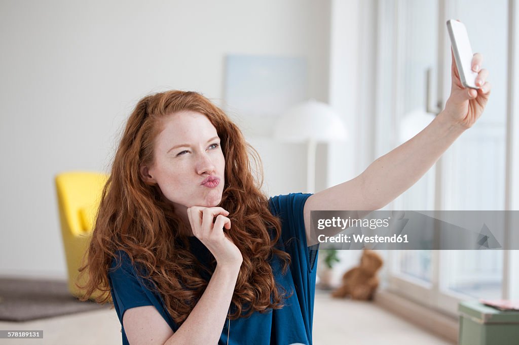 Young woman sitting in her living room taking a selfie with smartphone