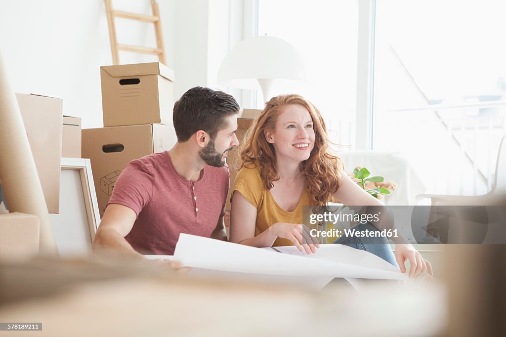 Young couple in new flat with cardboard boxes holding ground plan