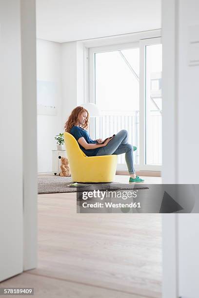 young woman sitting on yellow armchair in her living room - beautiful living room fotografías e imágenes de stock