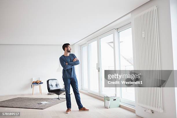 young man standing in his living room looking through window - sideways glance stock pictures, royalty-free photos & images