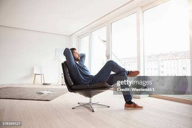 young man relaxing on leather chair in his living room - man living room stockfoto's en -beelden