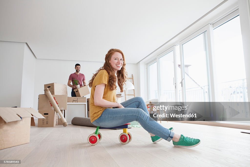 Young couple moving into new flat, woman sitting on toy cart