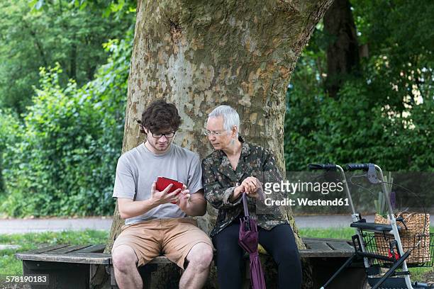 senior woman looking at young man with digital tablet on park bench - oma rollator stockfoto's en -beelden