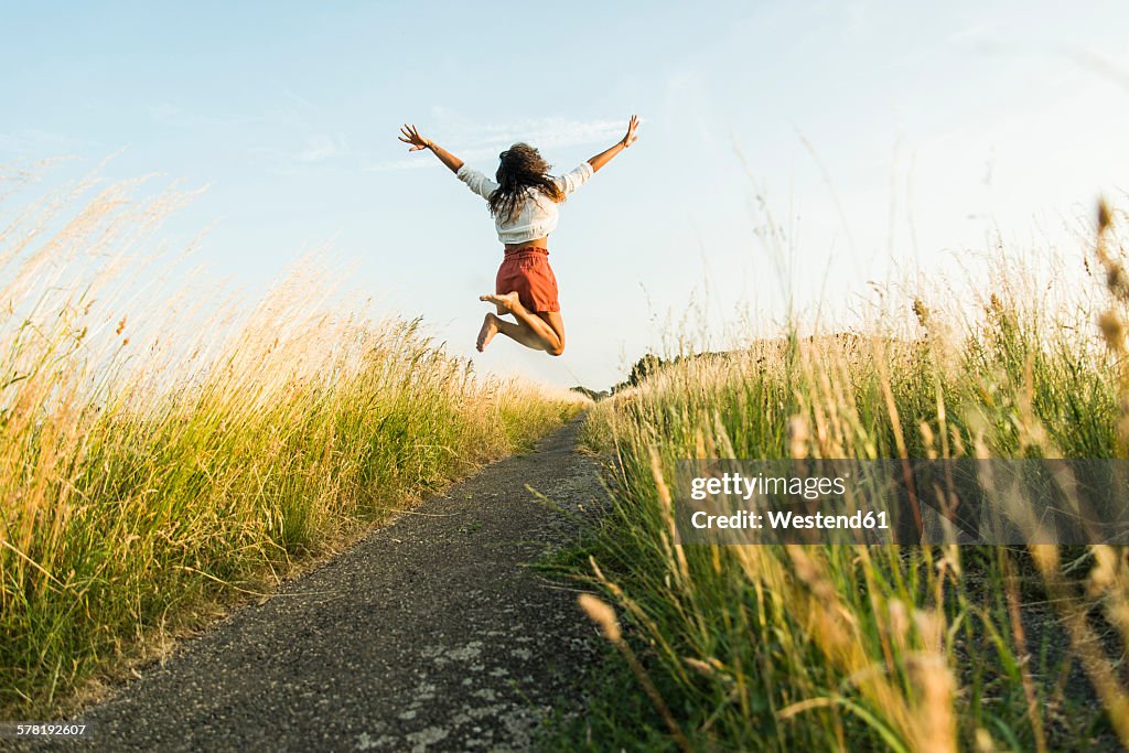 Enthusiastic young woman jumping on path in field