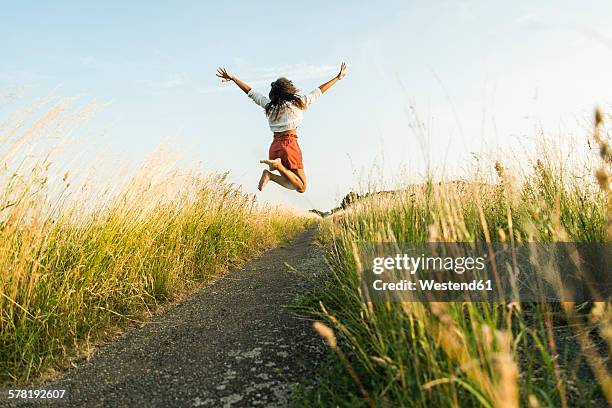 enthusiastic young woman jumping on path in field - euforie stockfoto's en -beelden