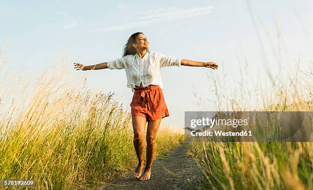 young woman standing with outstretched arms on path in field - barefoot women - fotografias e filmes do acervo