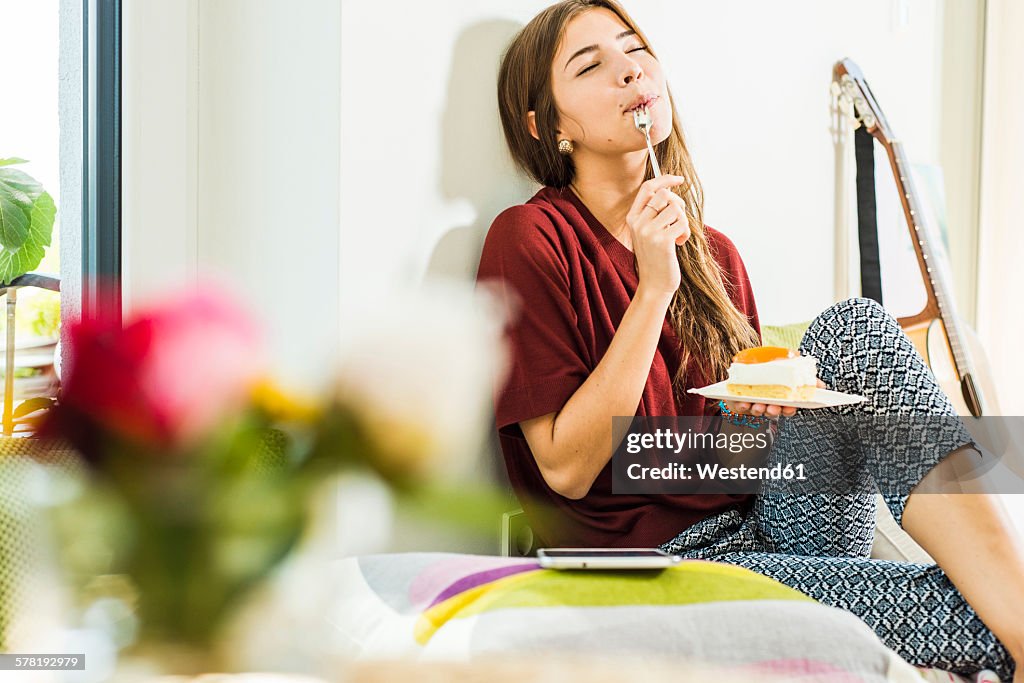 Young woman at home enloying piece of cake in bed