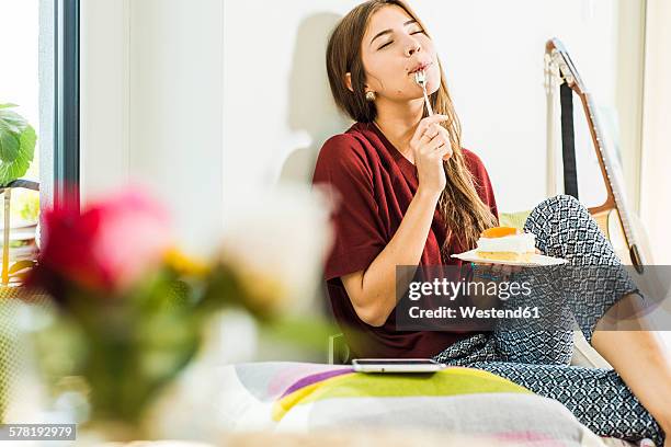 young woman at home enloying piece of cake in bed - kuchen stock-fotos und bilder