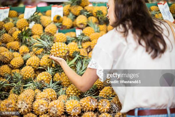 woman checking pineapples at fruit stall - tropical fruit stock pictures, royalty-free photos & images