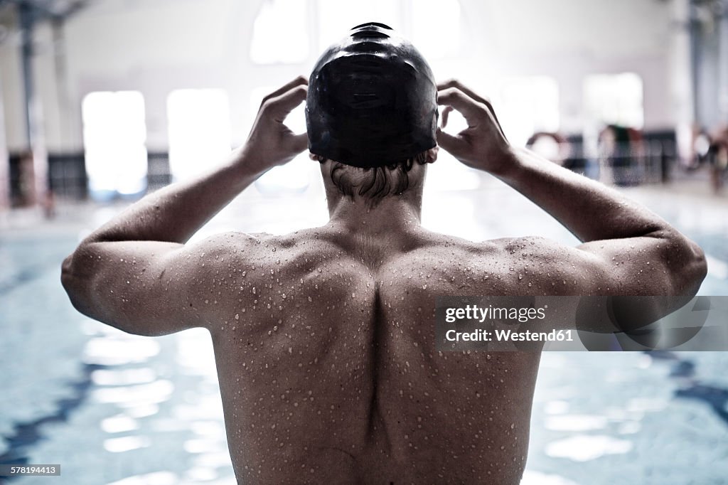 Swimmer in indoor pool putting on swimmming goggles