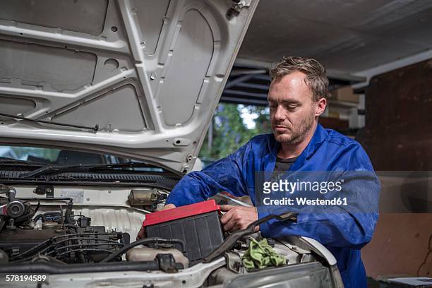 man working on car in home garage removing battery - autobatterie stock-fotos und bilder