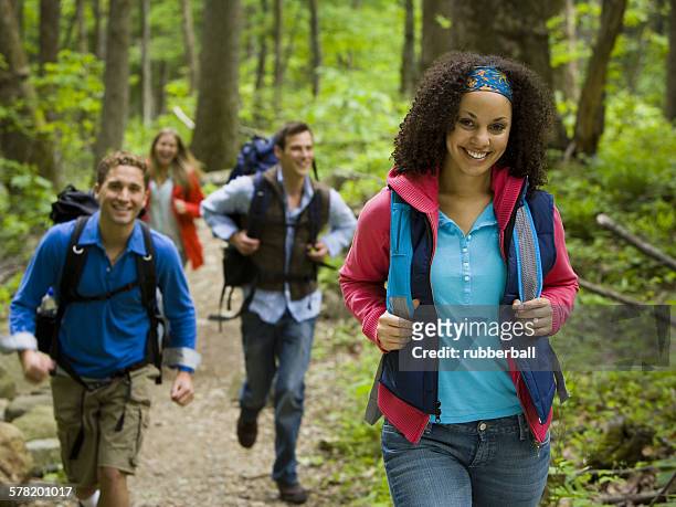 four young adults hiking in the forest - freundschaft fotografías e imágenes de stock
