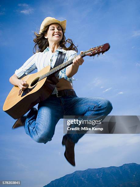 low angle view of a young woman jumping and playing the guitar - rayado photos et images de collection